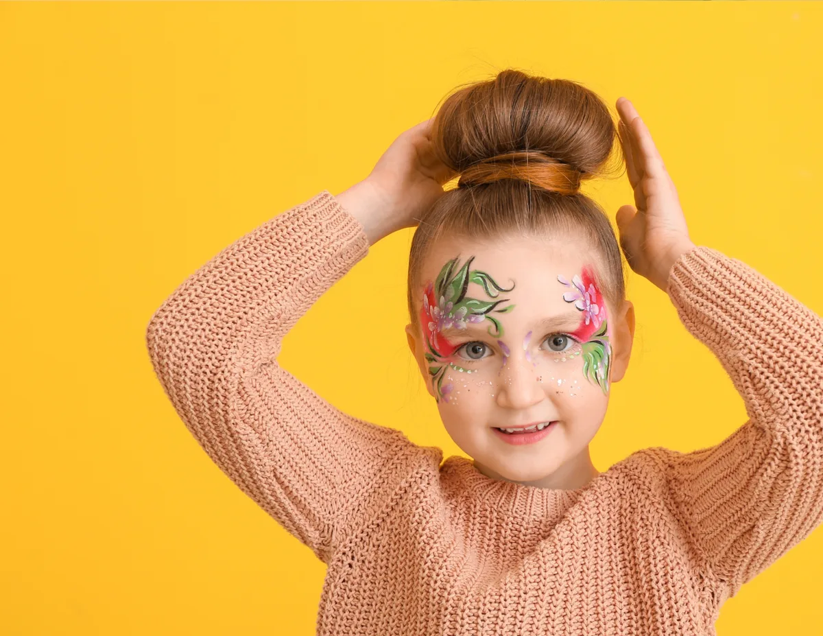 Girl with colorful flower face painting on a yellow background.