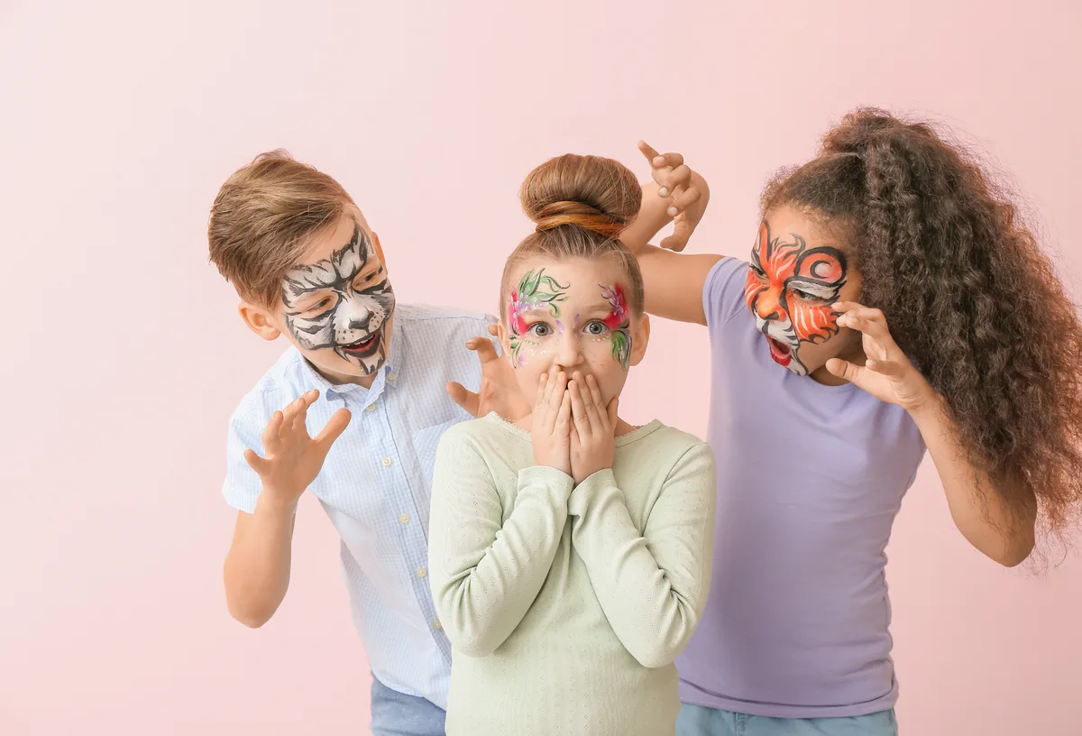 Three children smiling with colorful tiger, flower, and zebra face painting by Colory Faces.