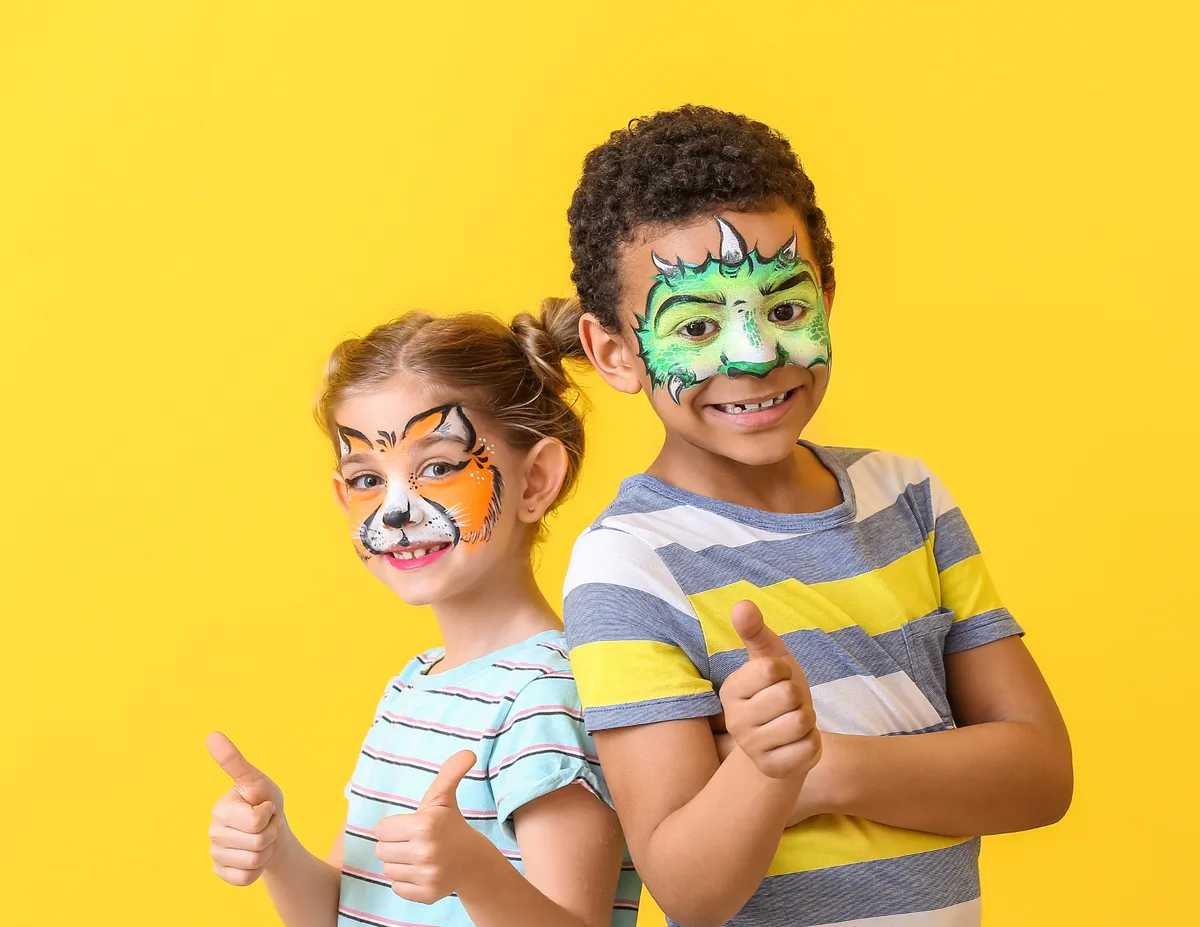 Two children with animal face painting on a yellow background.